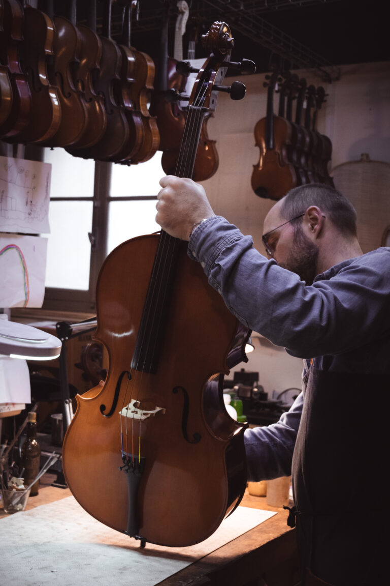 Photo d’un luthier travaillant le bois pour fabriquer un violon dans son atelier. Image illustrant le savoir-faire artisanal et la précision du travail manuel.