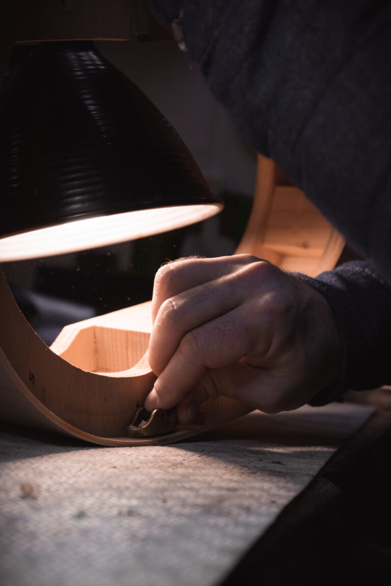 Photo d’un luthier travaillant le bois pour fabriquer un violon dans son atelier. Image illustrant le savoir-faire artisanal et la précision du travail manuel.