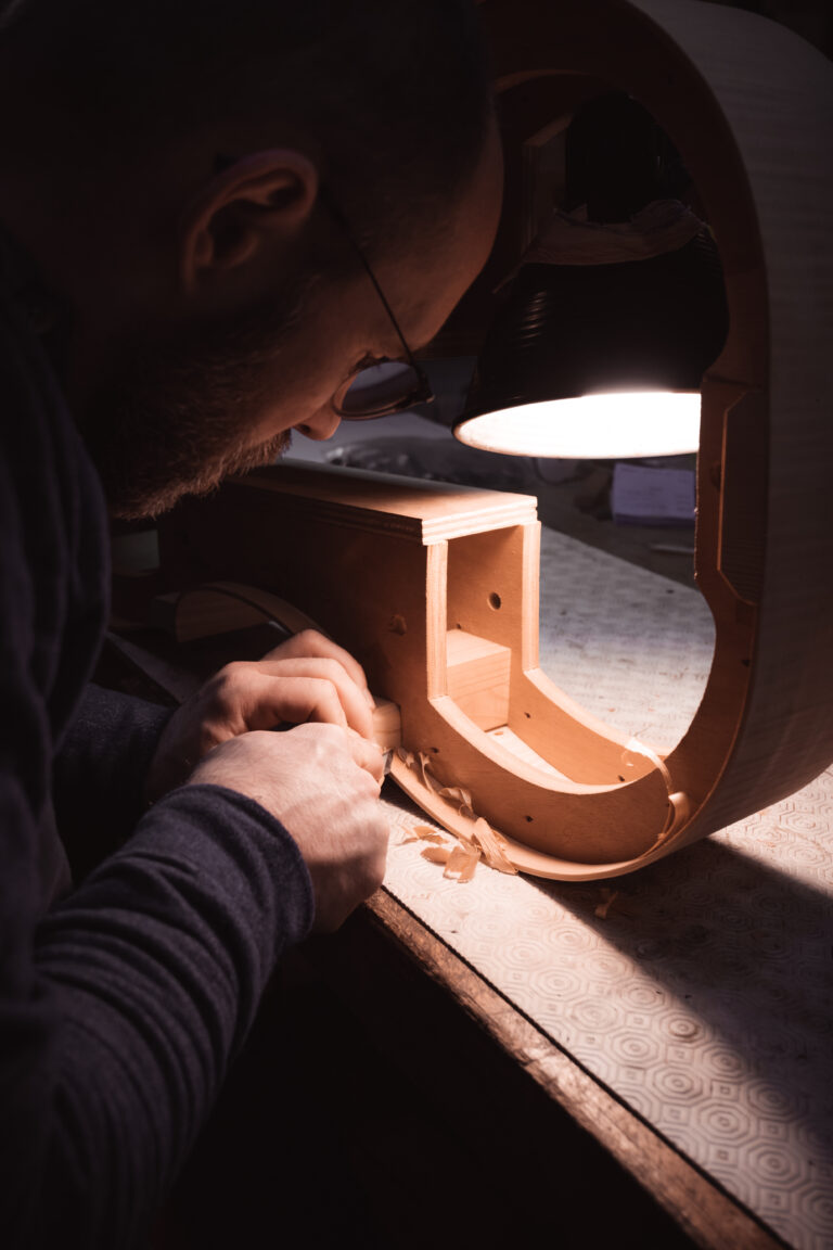 Photo d’un luthier travaillant le bois pour fabriquer un violon dans son atelier. Image illustrant le savoir-faire artisanal et la précision du travail manuel.