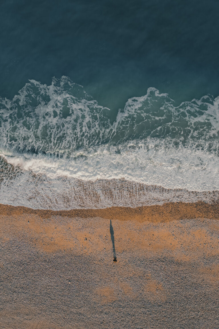 Image aérienne d’une vague se brisant sur la plage. Photo de paysage marin avec textures naturelles et couleurs apaisantes.